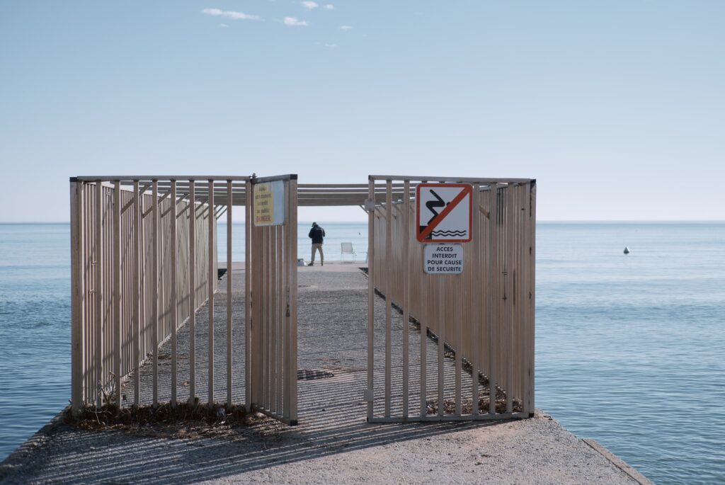 Un homme au bout d'une jetée face à la mer avec une cage ouverte en avant plan